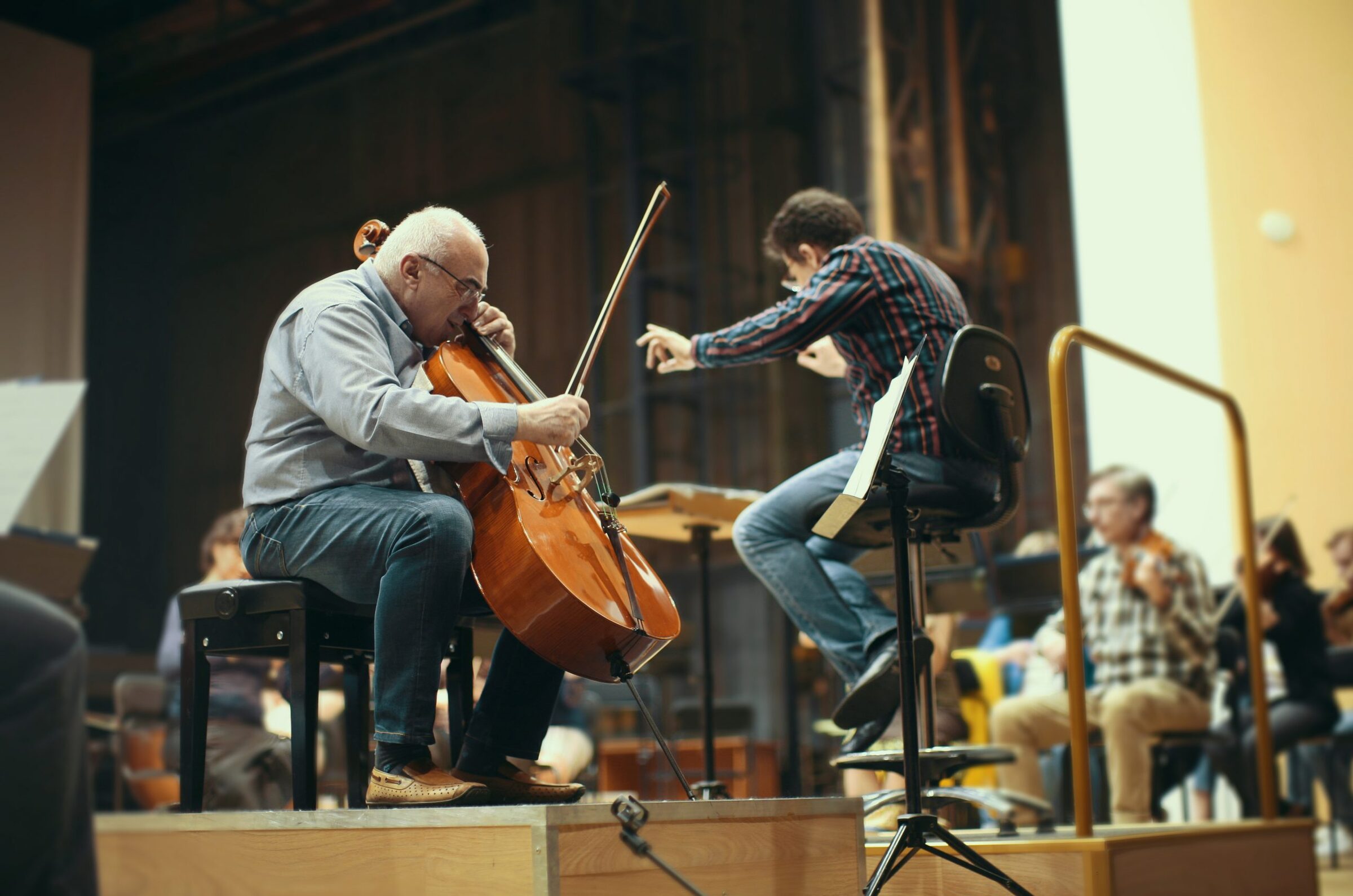 Alexander Kaganovsky playing the cello during an orchestra rehearsal, with the conductor beside him