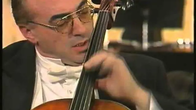 Video still: close-up of a cellist in glasses and a white bow tie, head turned to the side as he bows the cello